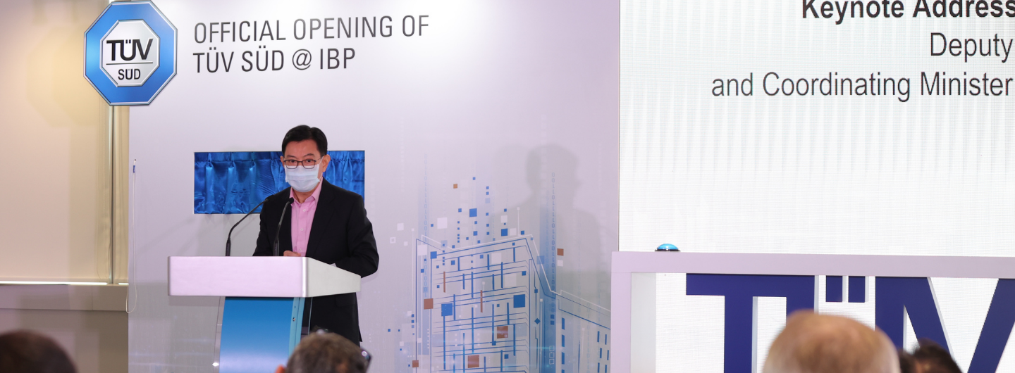 Asian man wearing a mask at podium with "TÜV SÜD" sign.